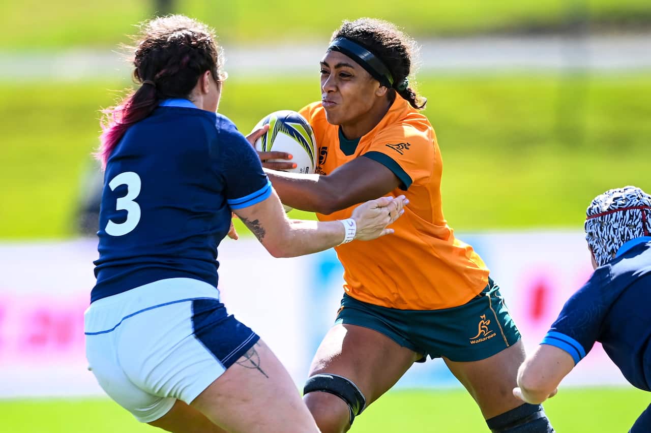 A woman in a gold rugby jersey tackled by a woman in a blue rugby uniform