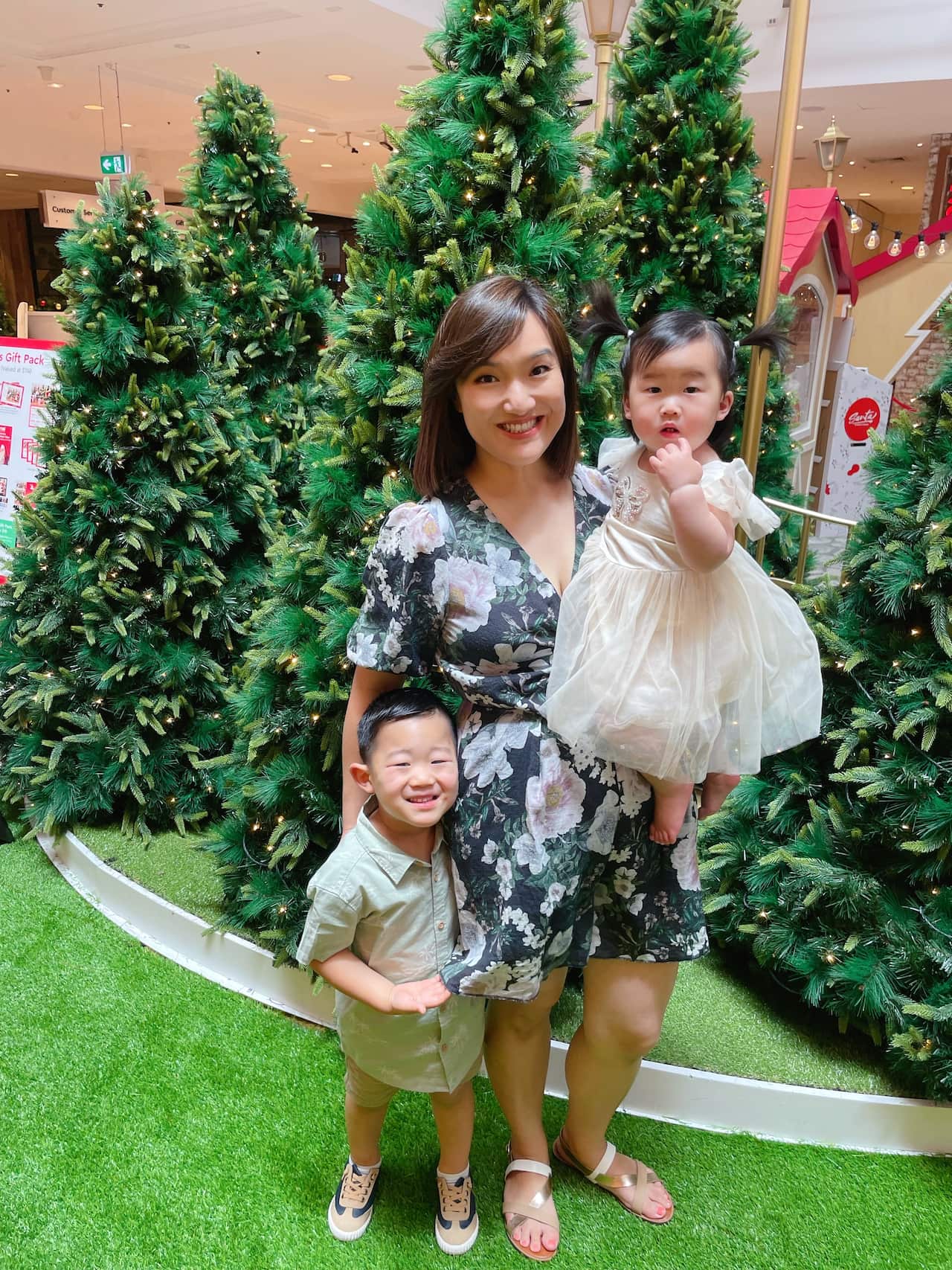 A woman holding a baby in her arms and cuddling her son in front of some Christmas trees