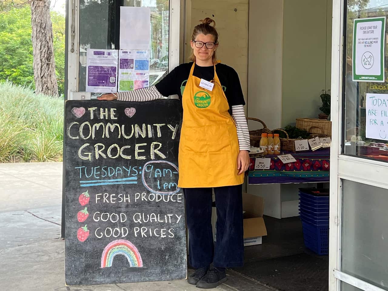 A woman in a yellow apron standing next to a chalkboard