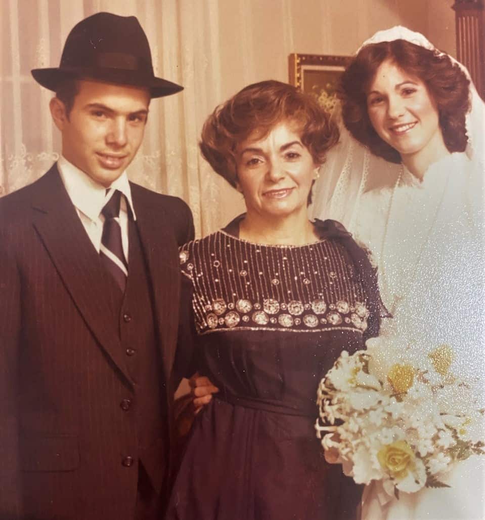 A young man in a hat stands next to a woman in a brown dress and another woman in a wedding dress.