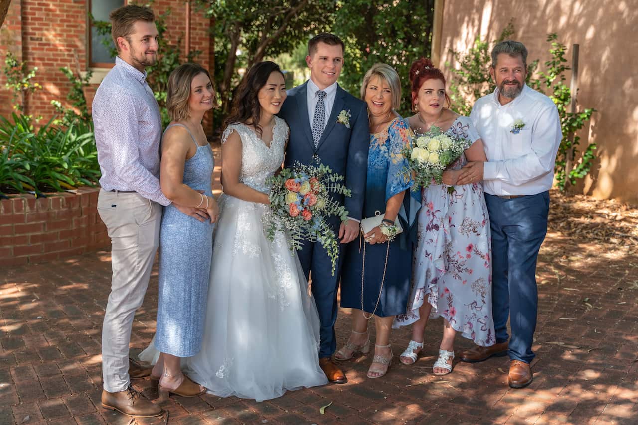 Seven members of a family stand together and smile at a wedding, with the bride and groom in the centre of the picture.