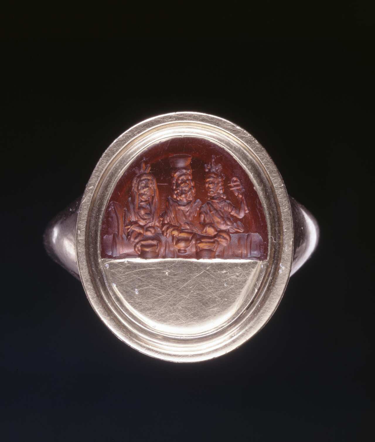 A silver ring with a brown artwork depicting three ancient figures.