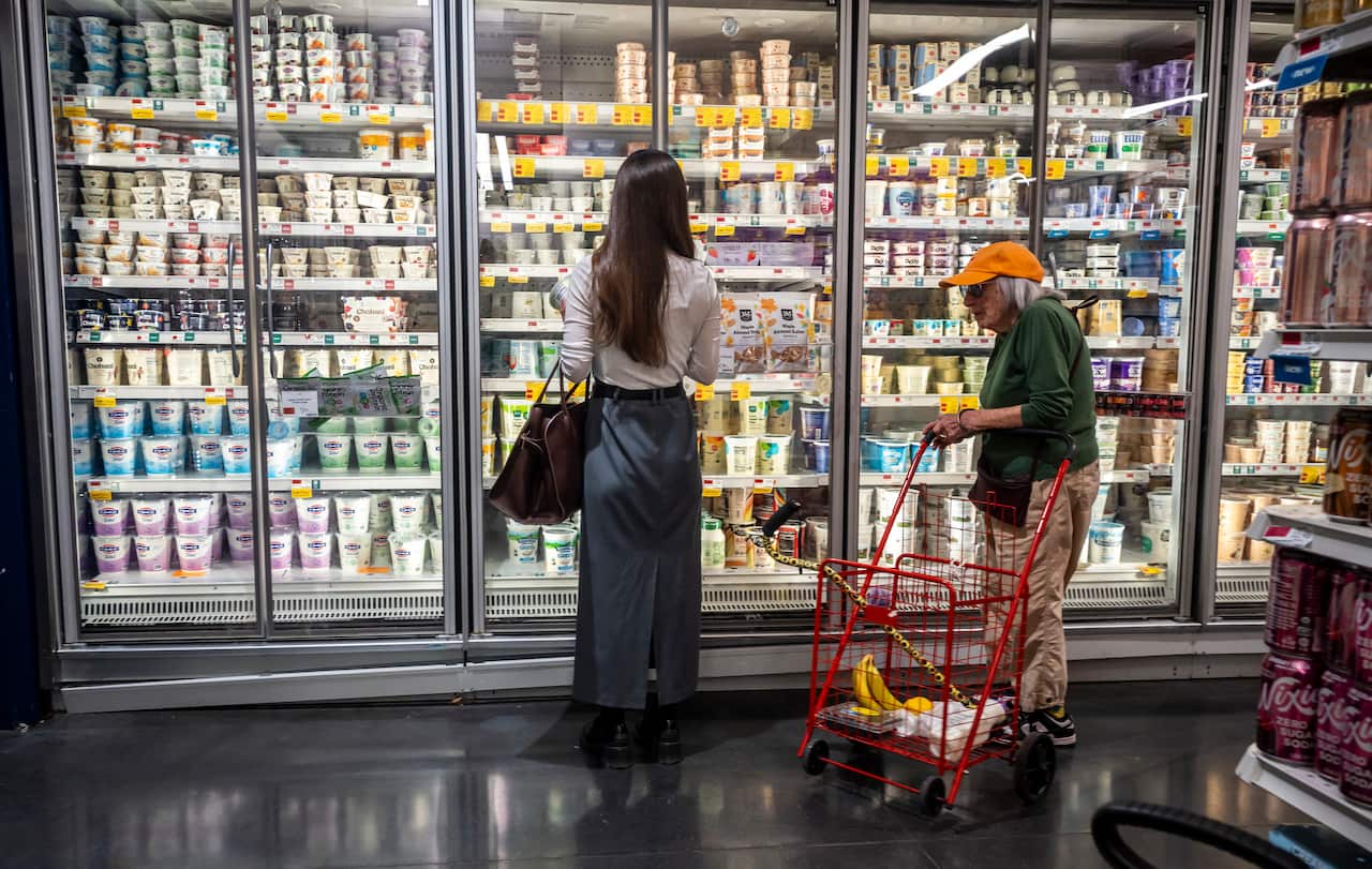 Two women standing next to a fridge in a grocery store.