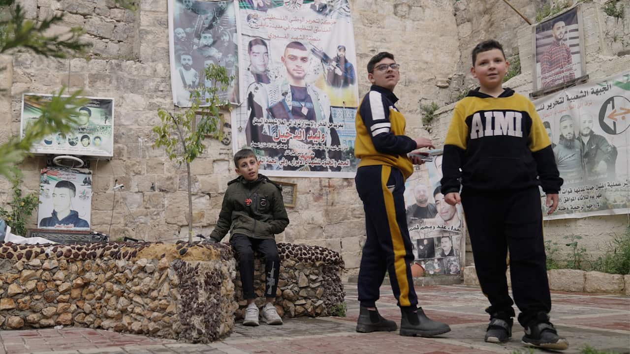 Three young boys standing in a yard with posters of men hanging on walls 