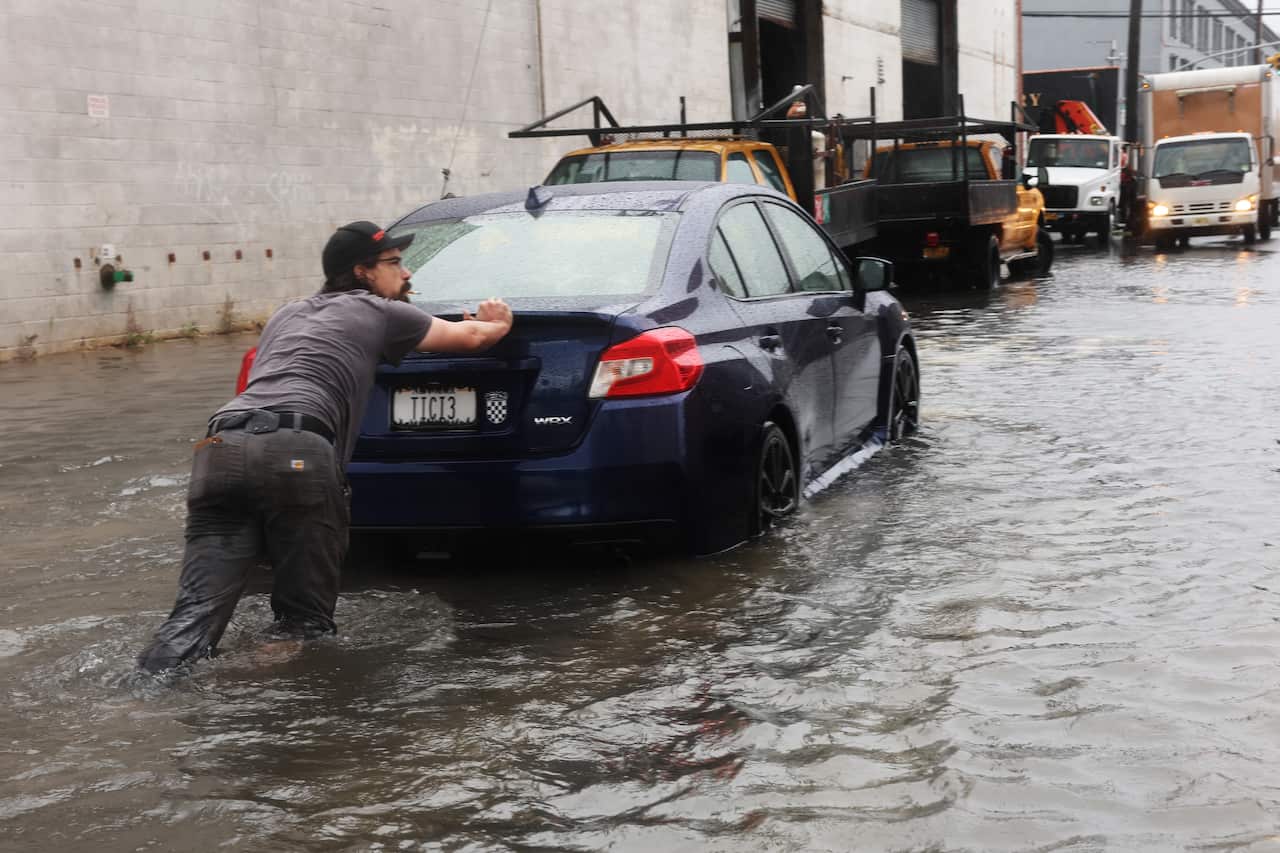 A man pushing a car along a flooded street.