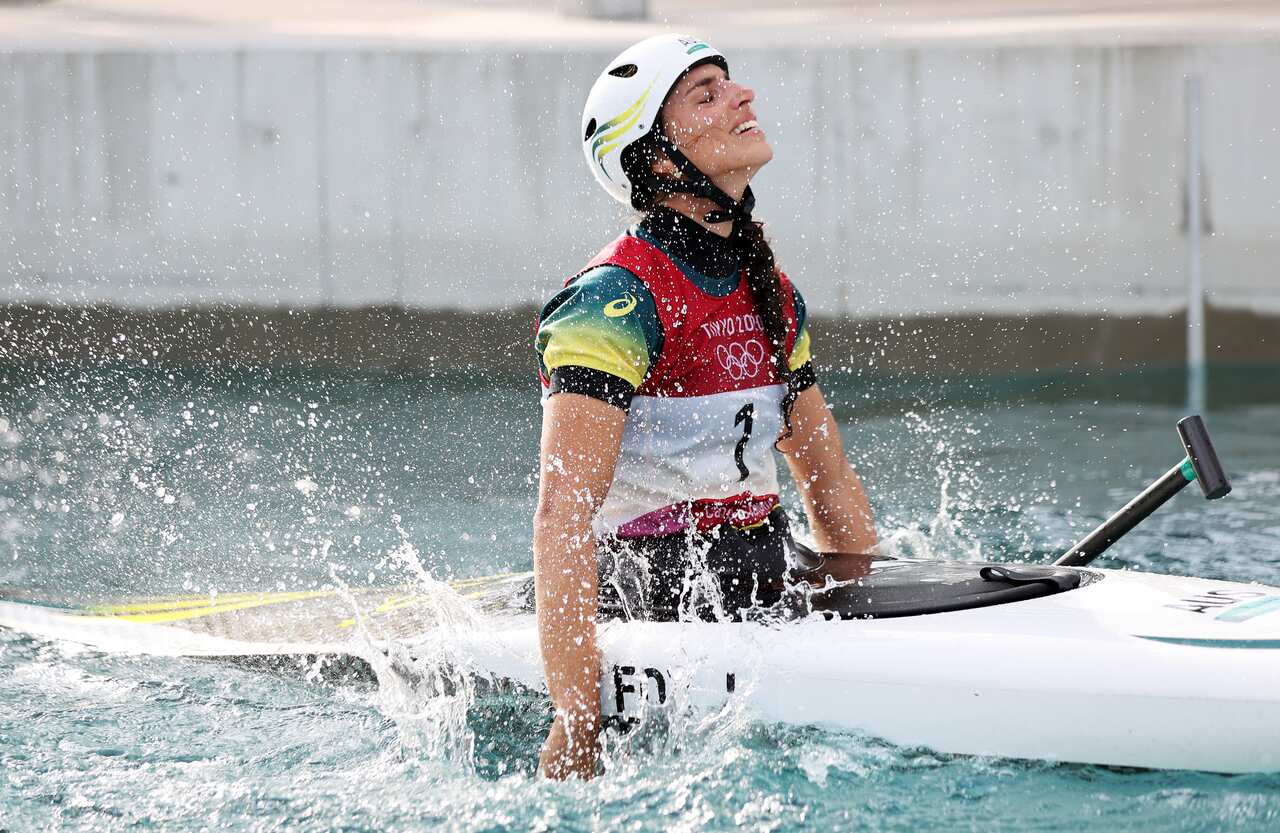 A woman in a kayak wearing a helmet splashes her hands into the water.