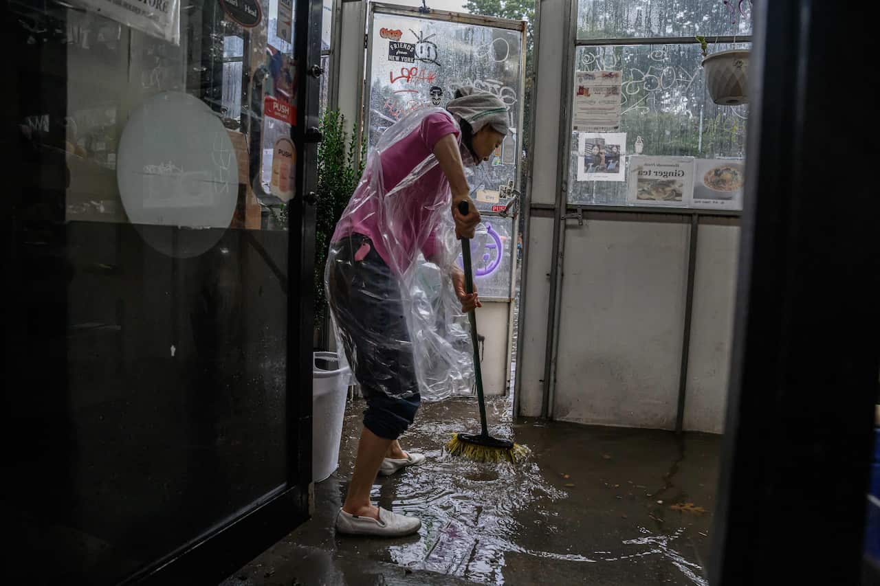 A woman wearing a poncho sweeping water from her shop.