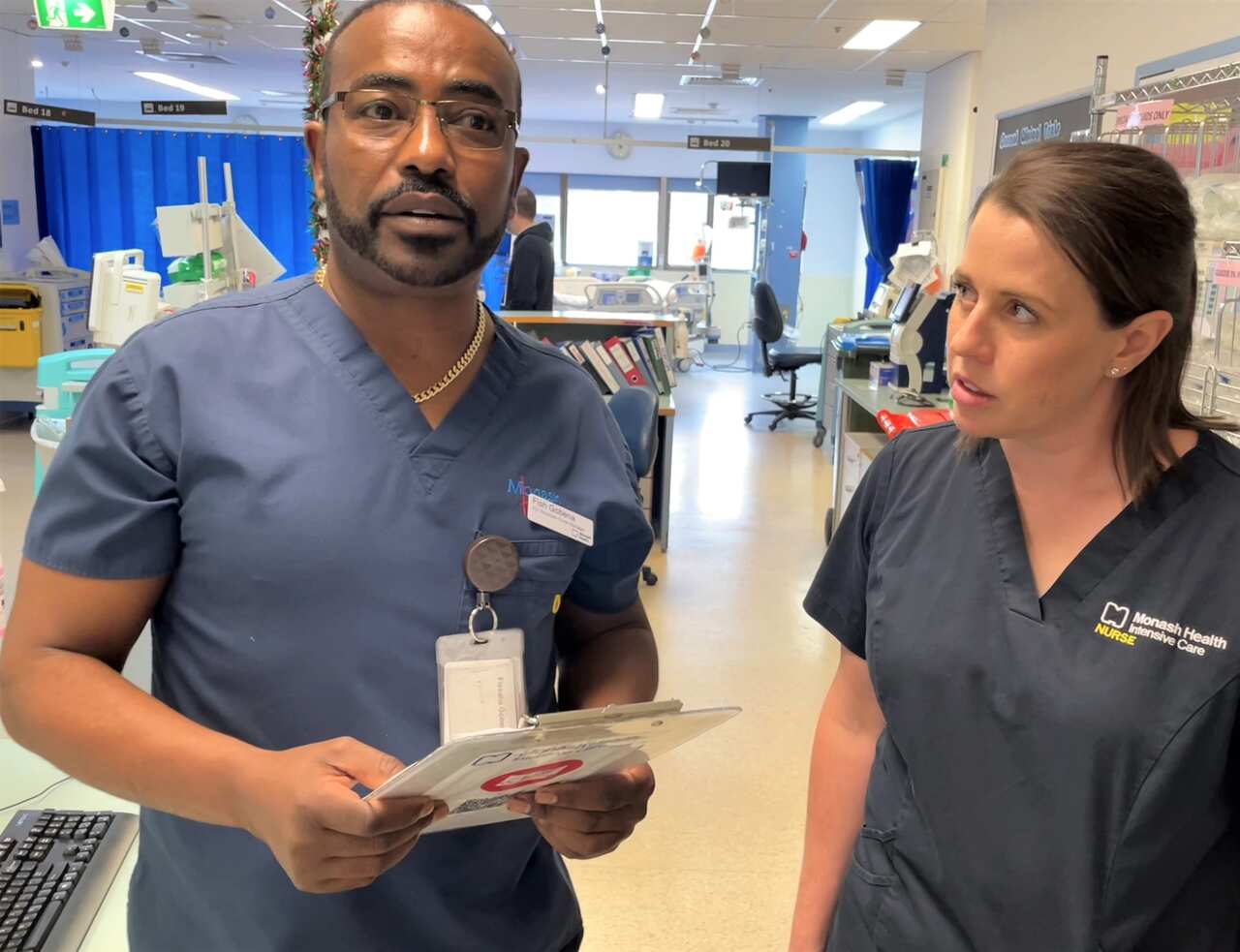 A man in a blue uniform stands holding a clip board next to a woman in a blue uniform.
