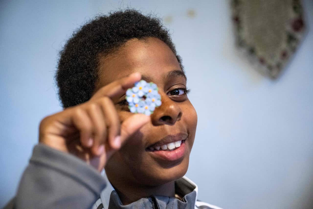 Boy smiles and looks through a blue and yellow Mayflower pin. 
