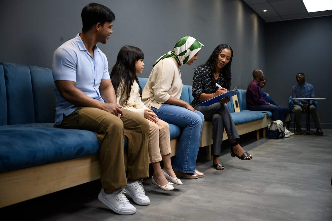 Full length, wide shot nurse fills in form with family sitting in hospital waiting room