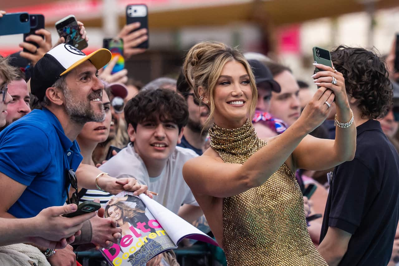Delta Goodrem wearing gold dress taking photo with man in crowd.