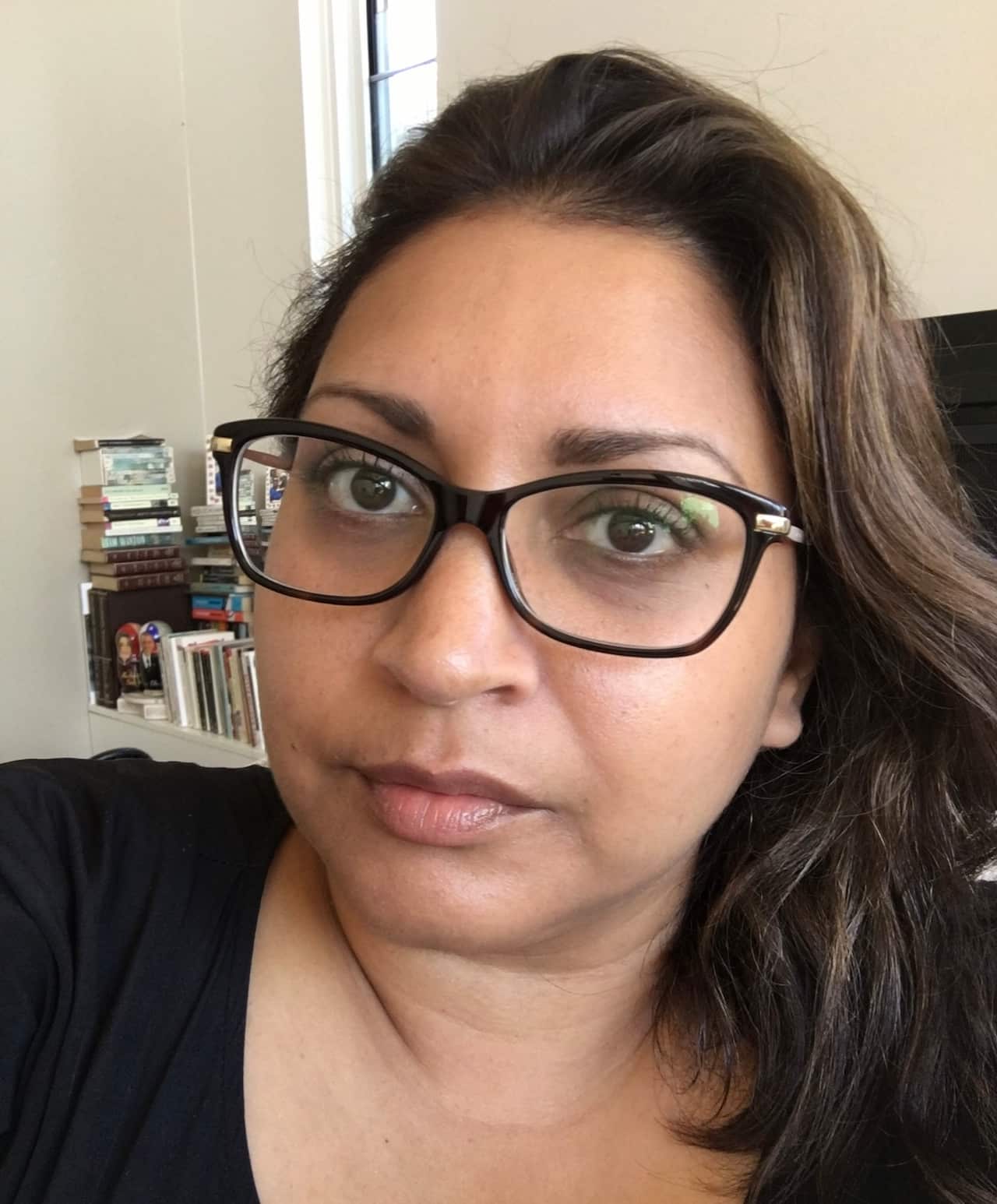 A selfie of a woman with dark hair and glasses with a neutral expression on her face.
