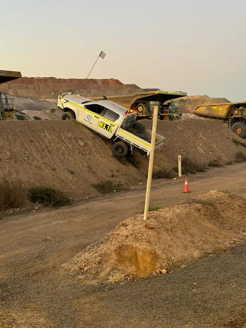 A ute backs dangerously over a dirt embankment.