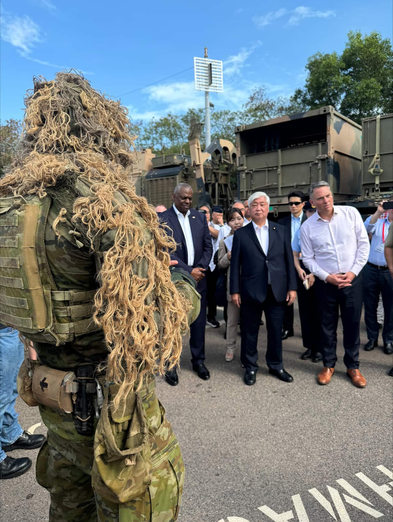 Three men stand before a man in combat uniform