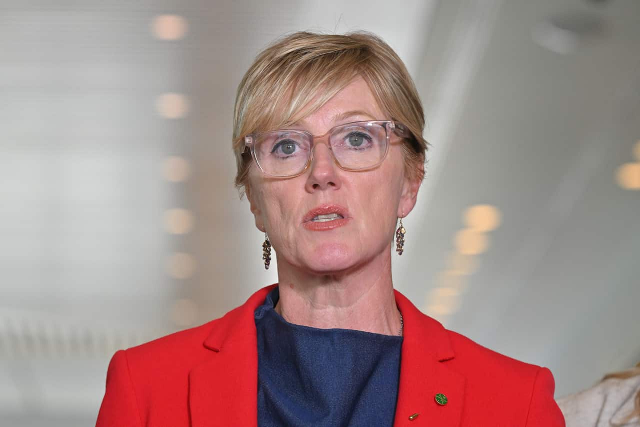 A woman with short blond hair, wearing a red blazer and blue top.