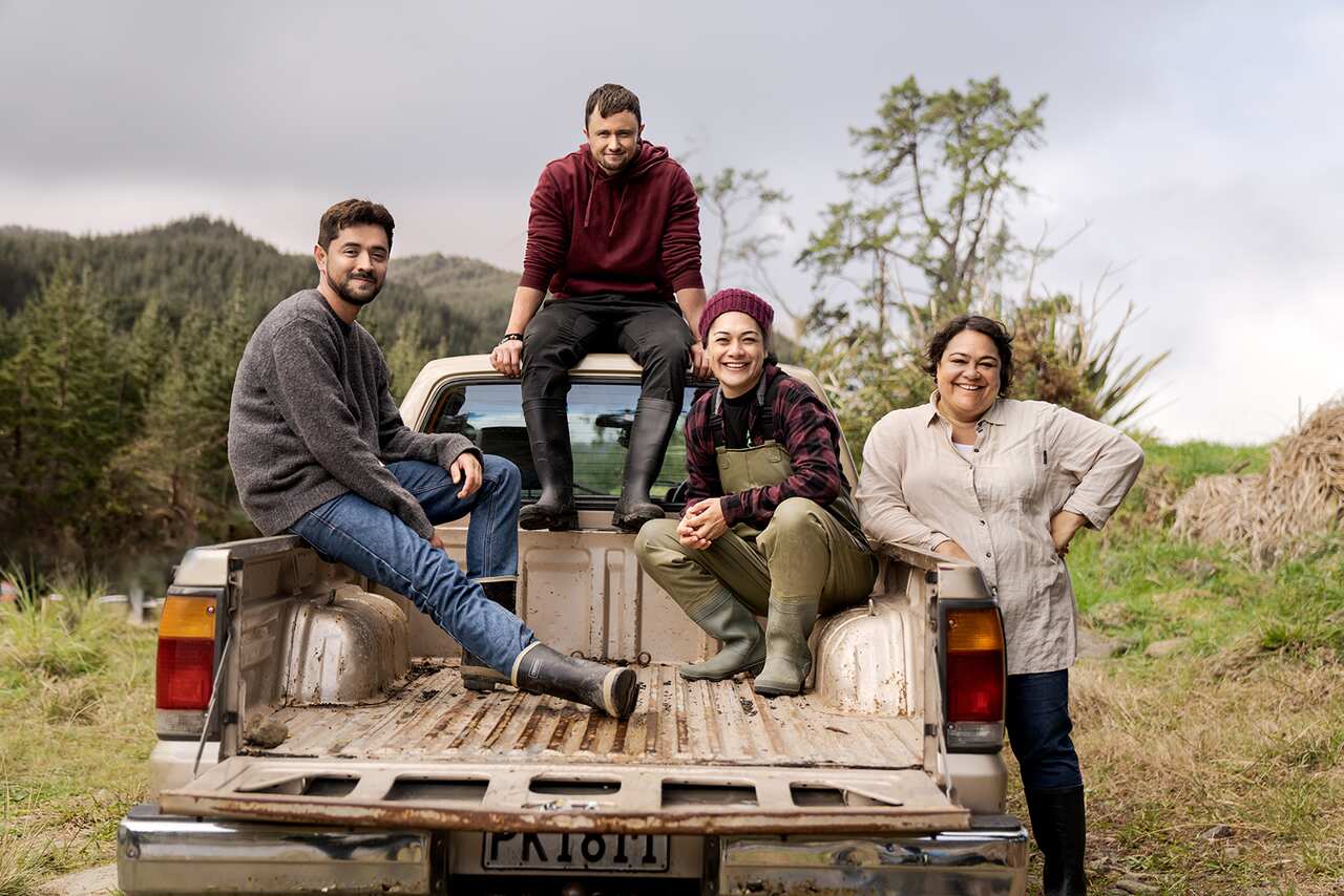 A ute is parked facing away from the camera. Two people sit in the back, another sits on the cabin top, and a fourth leans against one side of the tray. They are all smiling. 
