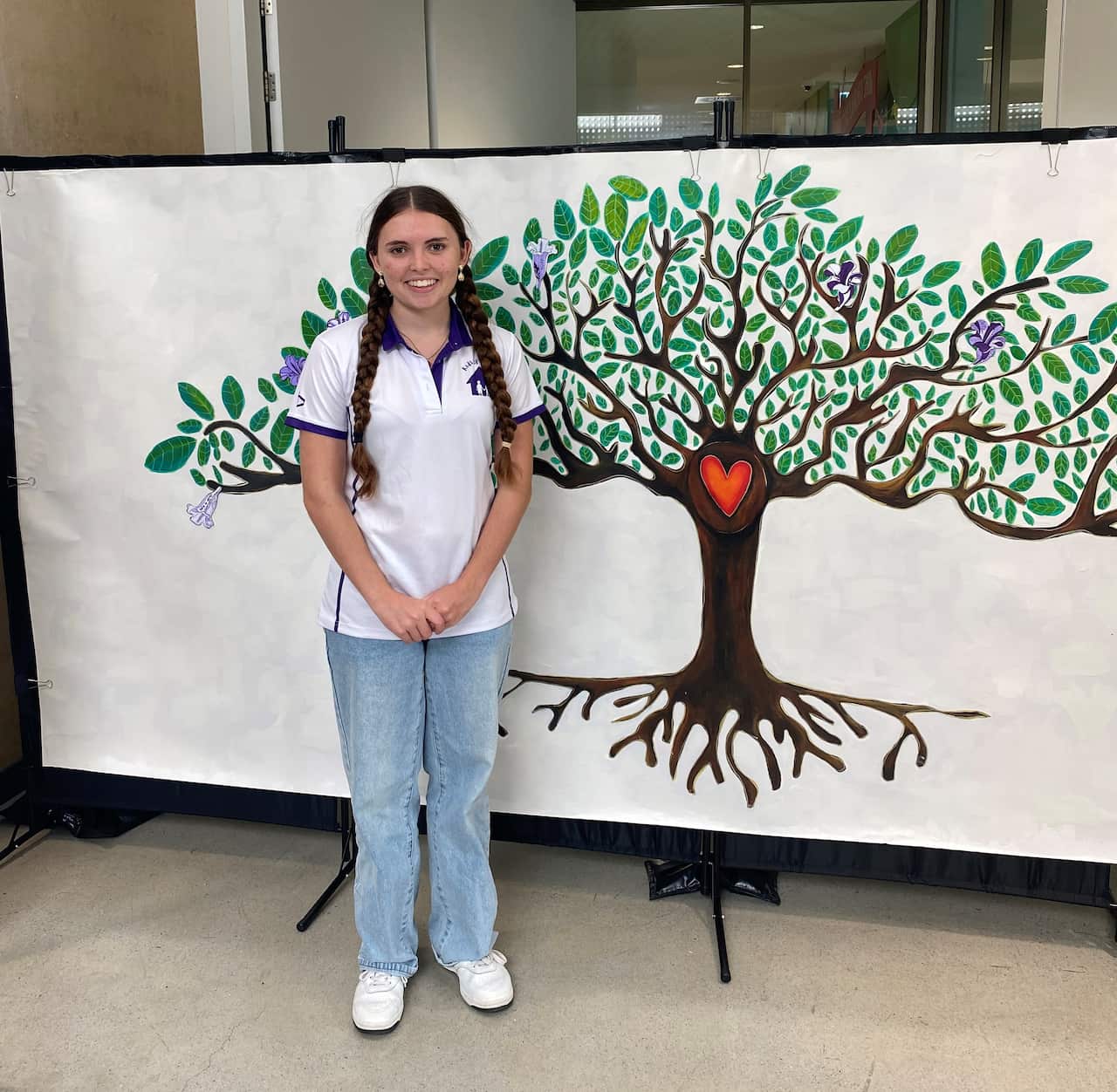 A young woman with brown hair wearing jeans and a white polo shirt smiles at a camera.