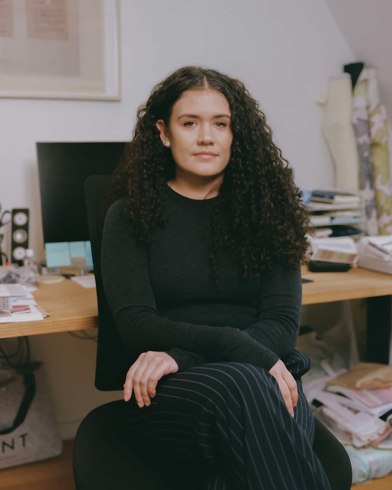 A woman with curly hair, wearing an all black outfit, is sitting inside a room.