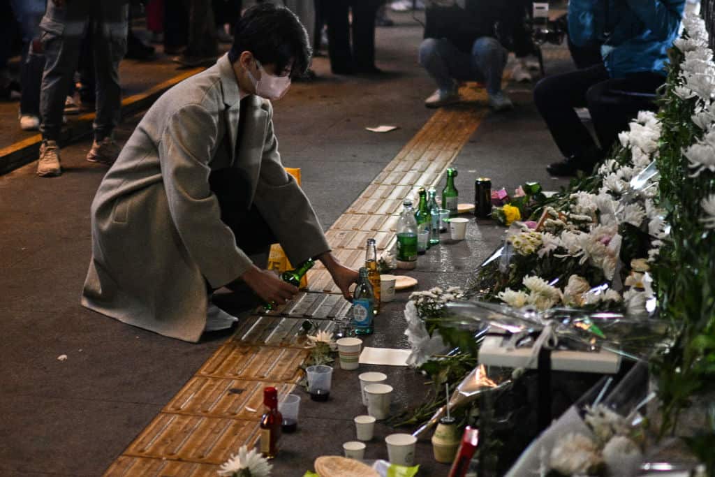 A man pours an alcoholic beverage in tribute to those who were killed in a Halloween stampede at a makeshift memorial outside the Itaewon subway station.