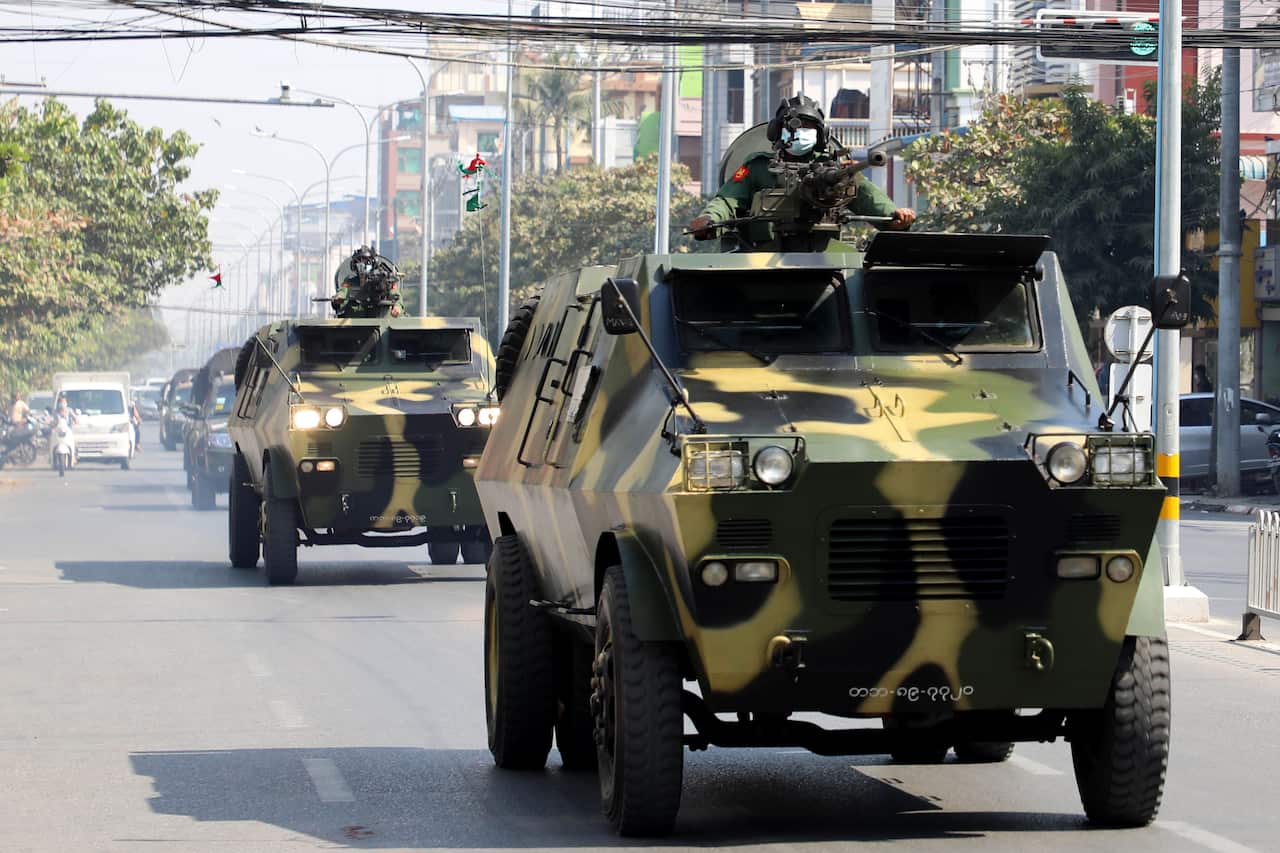 Soldiers in armoured carriers drive down a street