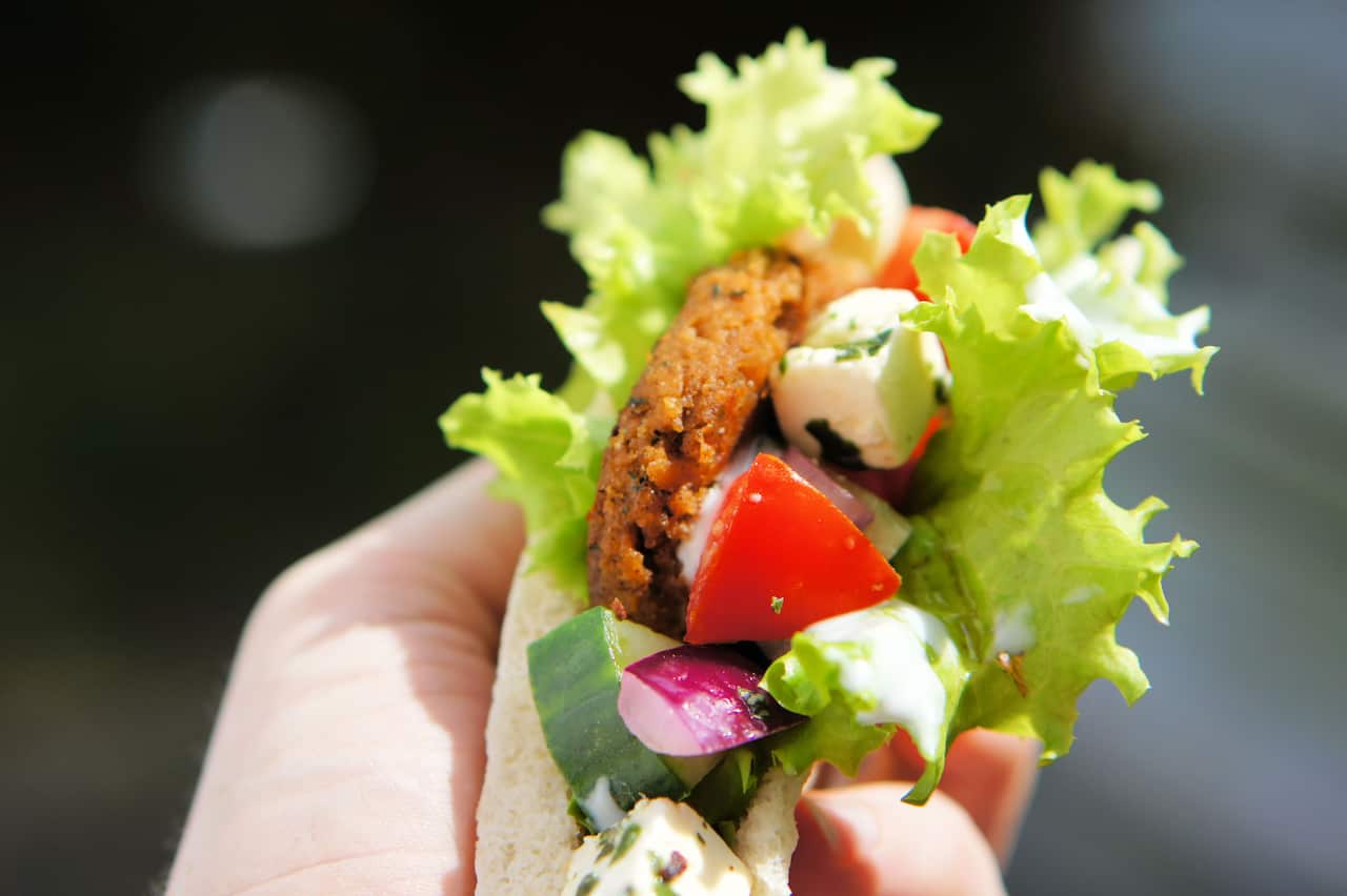 A gyro made from insect burger patties, inside pita bread being held in one hand.