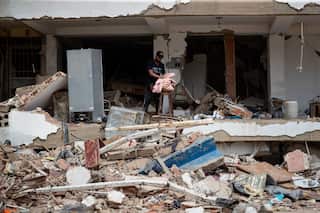 A man collects leftovers as he stands amid the rubble of a building destroyed by earthquakes.