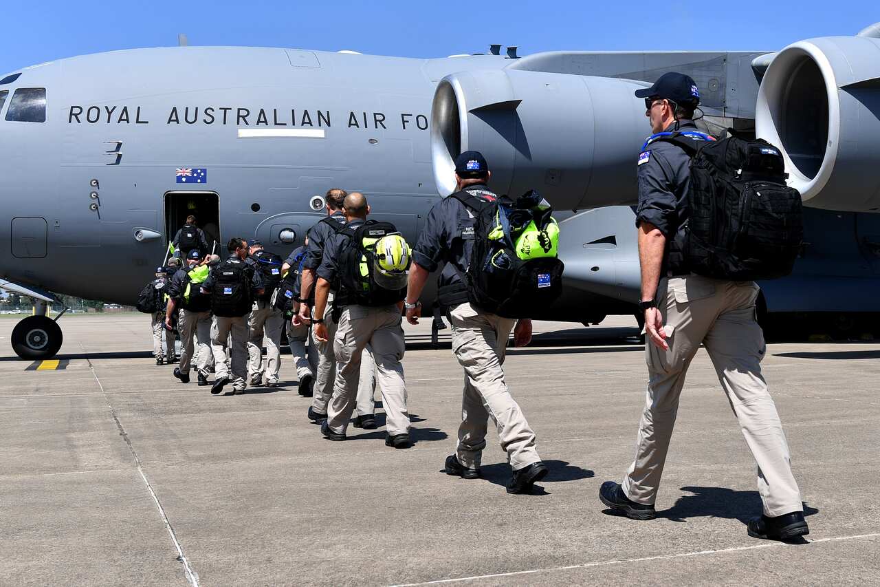A line of people walking towards a large grey plane that has Royal Australian Air Force written on its side