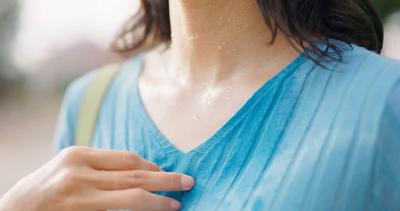 A woman's sweaty neck and chest up close. She's wearing a blue top, has dark hair, and has her right hand on her chest.
