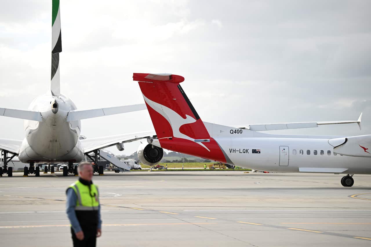 A Qantas plane on the tarmac at the airport. An airport worker in high-vis is in the foreground.