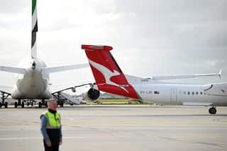 A Qantas plane on the tarmac at the airport. An airport worker in high-vis is in the foreground.