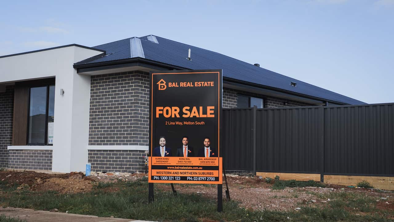 A for sale sign in front of a new house. The sign features photos of three real estate agents and includes their contact information.