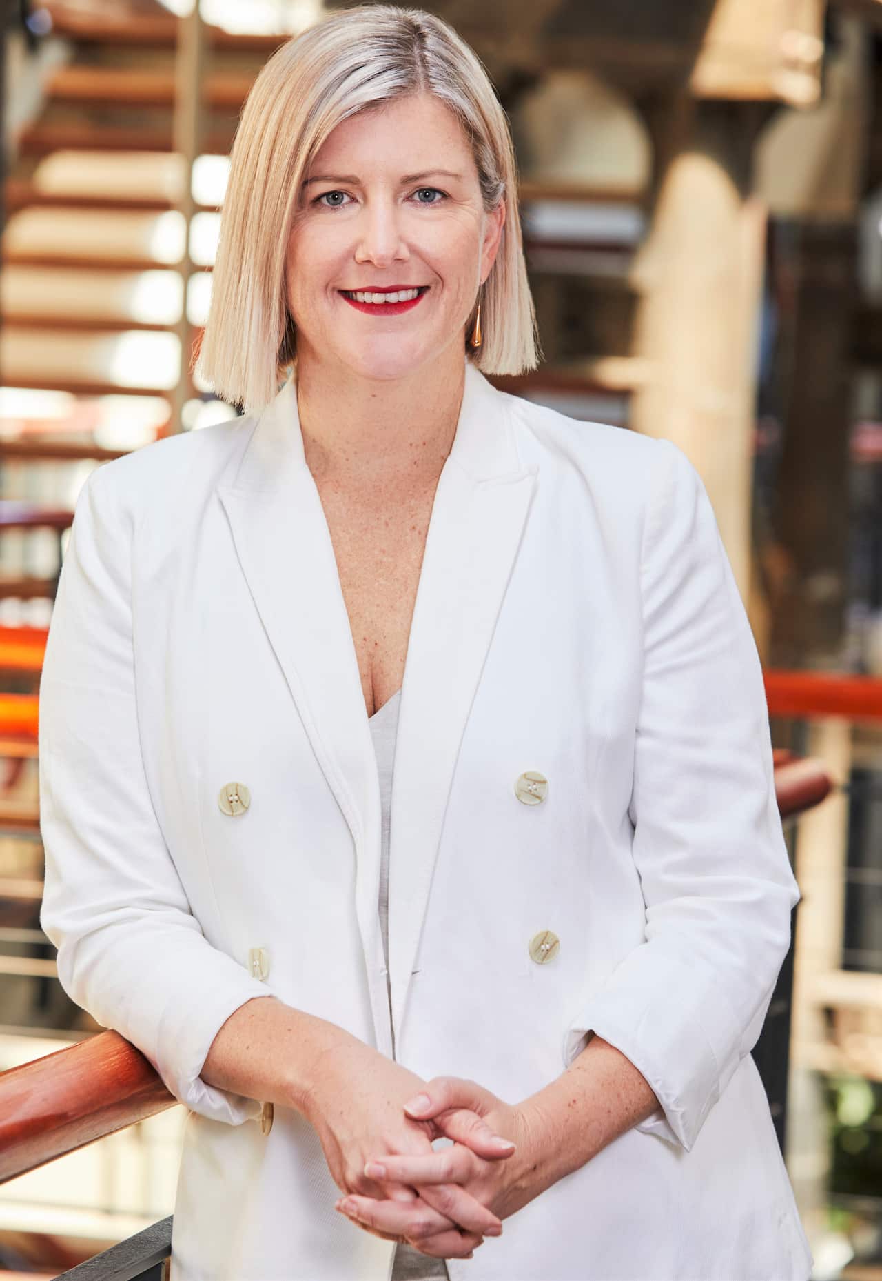 A woman in a white blazer stands with hands clasped.