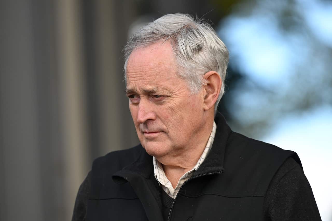 A man with grey hair wearing a black coat.