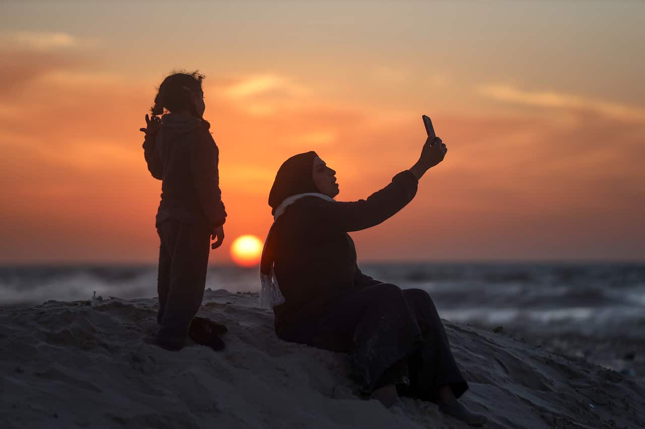 A woman taking a selfie with a child on a beach at sunset.