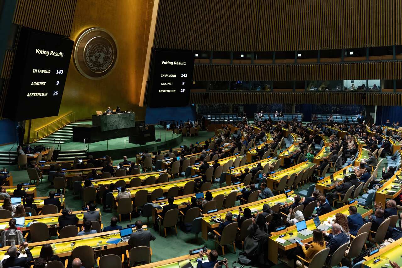 Members of the United Nations General Assembly look at the results of a vote displayed on a screen while seated.
