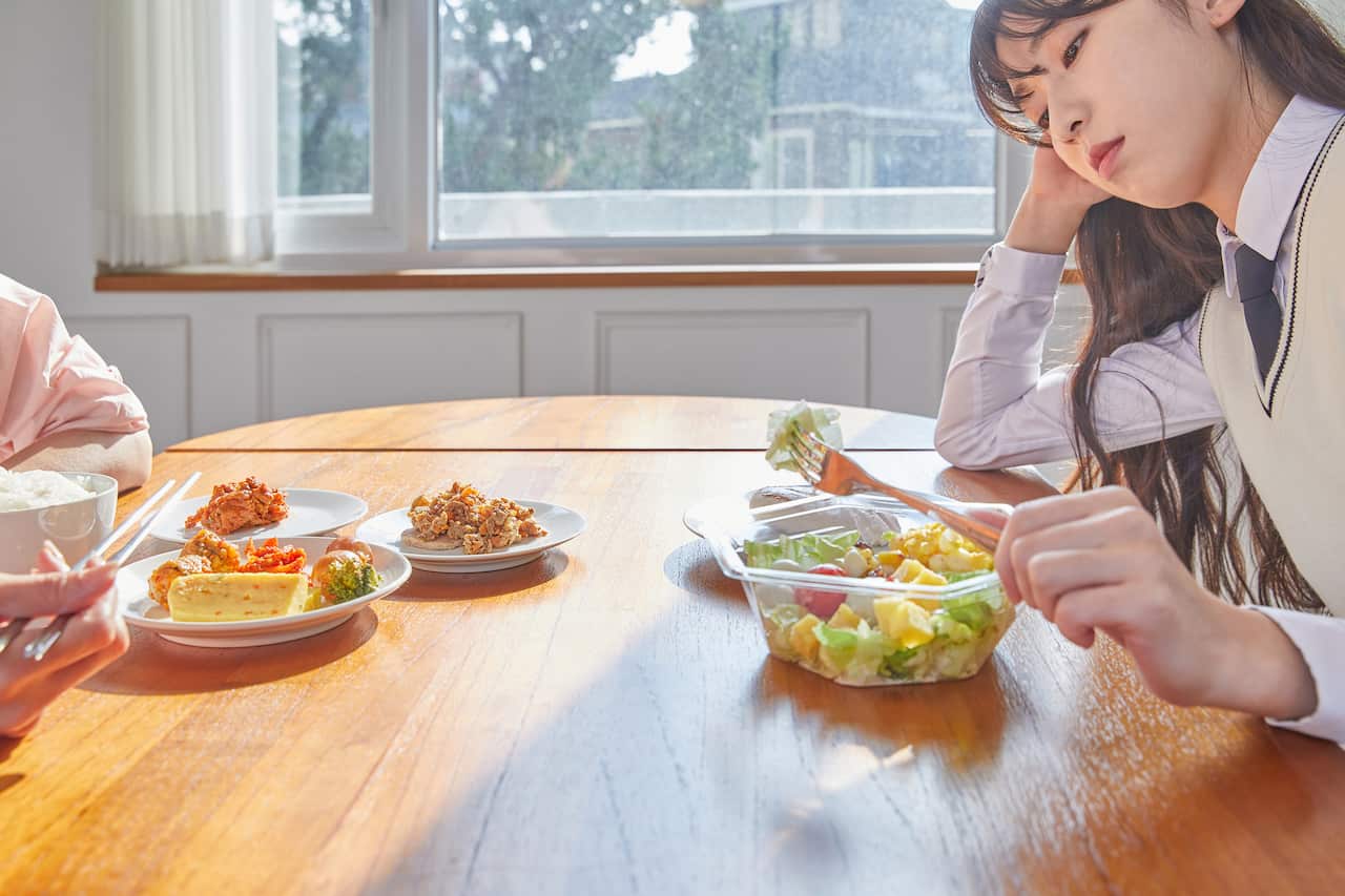 Asian woman sitting at table staring at salad uninterested in food