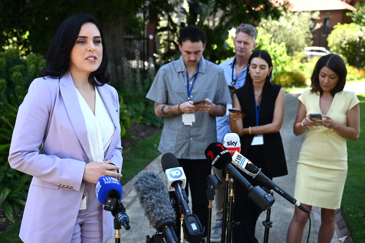 A woman speaks at a press conference with four media members on her left side.