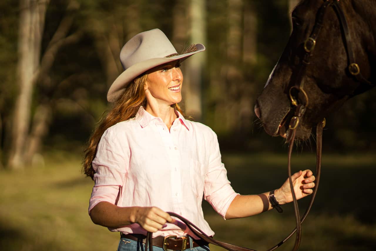 A woman in a stetson hat tends to a horse.