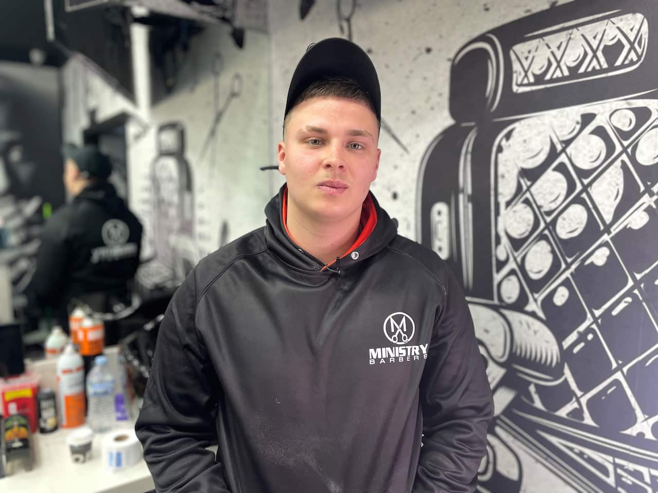 A young boy stands in a barber uniform and a hat. 