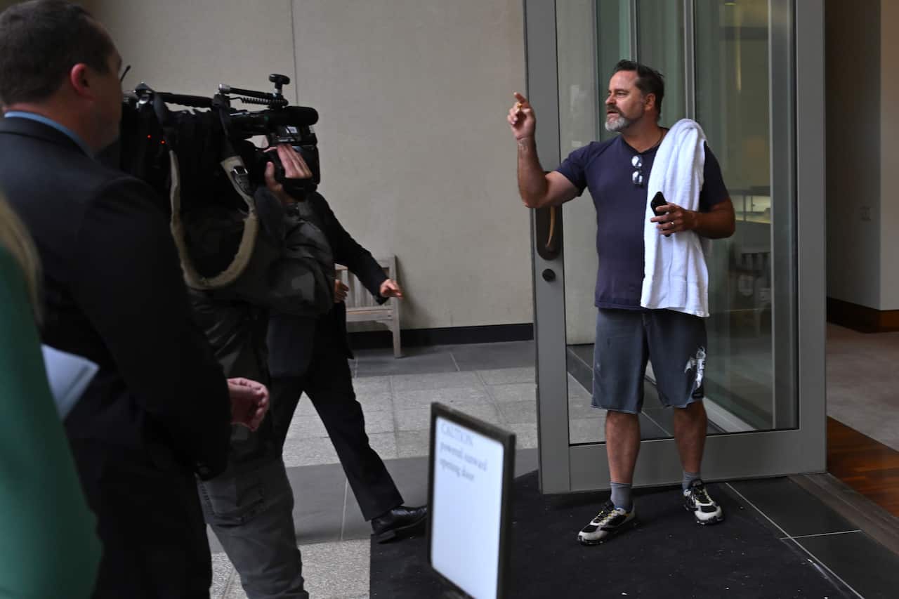 Greens Senator Peter Whish-Wilson yells while standing by a glass door near a courtyard in parliament house.