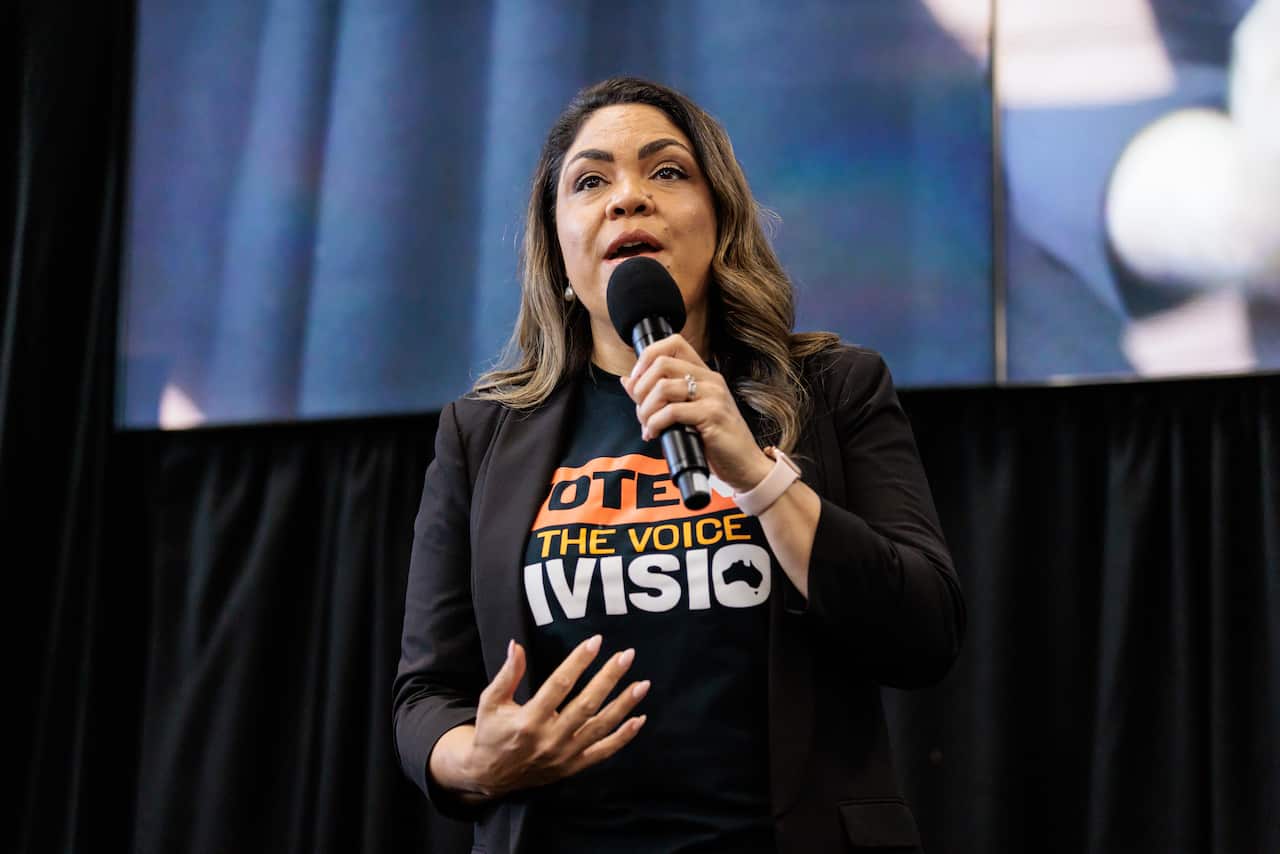 A woman in a black T-shirt and blazer holding a microphone on stage.