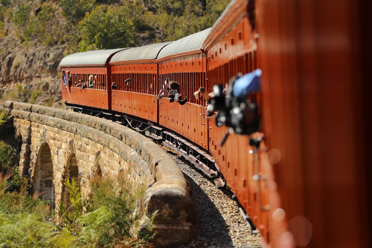 An old fashioned train being driven on tracks next to a cliff.