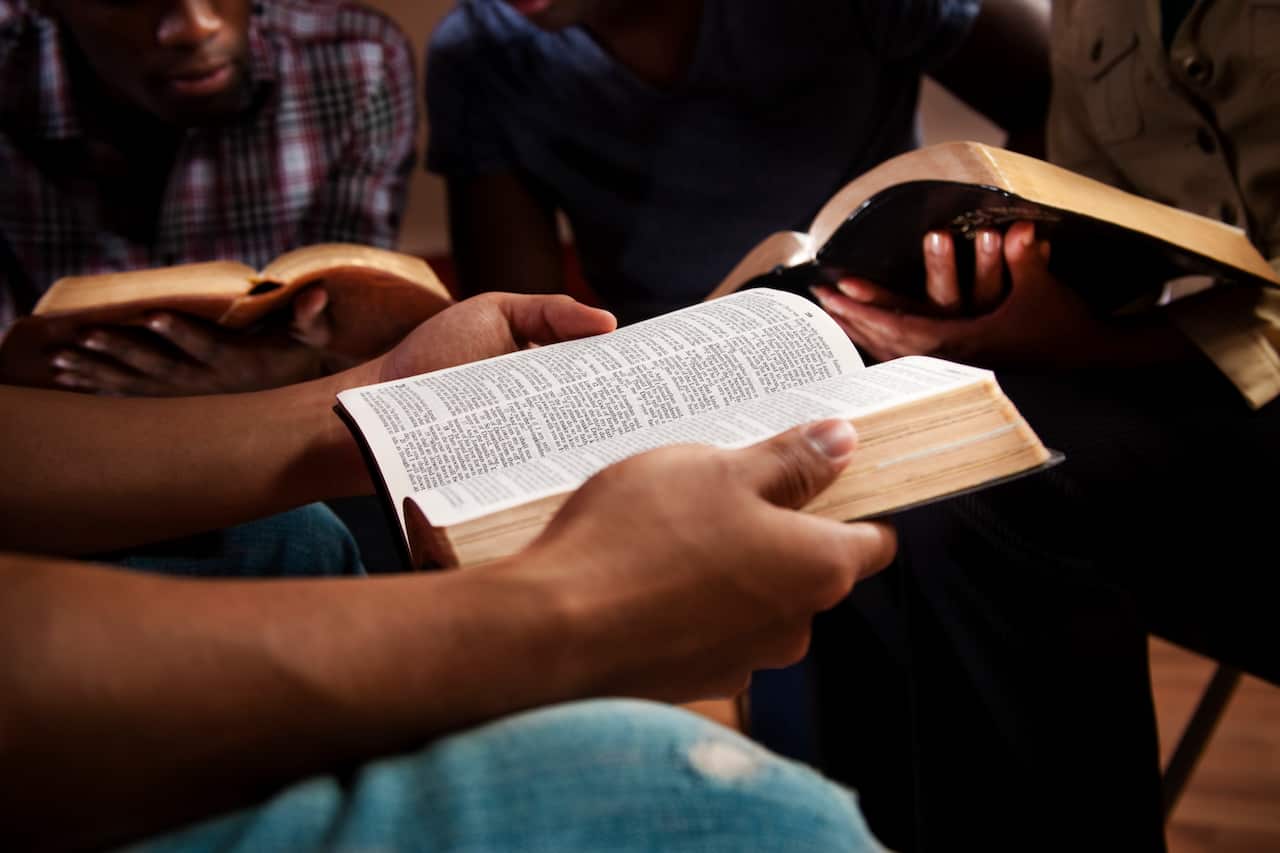 Pairs of hands holding bibles out in front reading.
