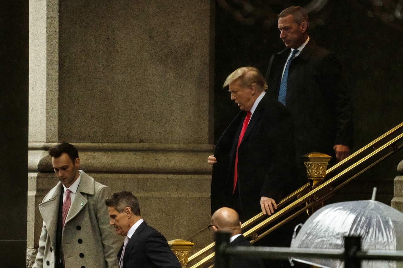 Donald Trump walking down a flight of stairs with other men around him.