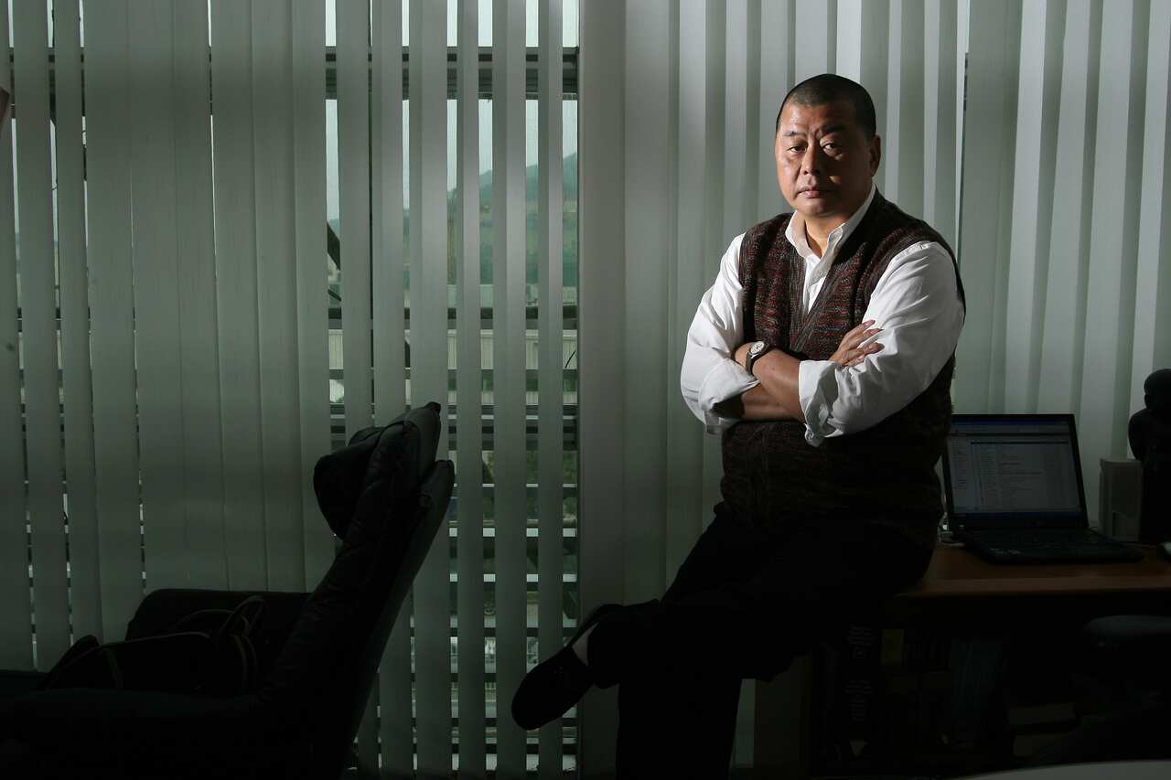 A man sits on the edge of a desk with his arms crossed.
