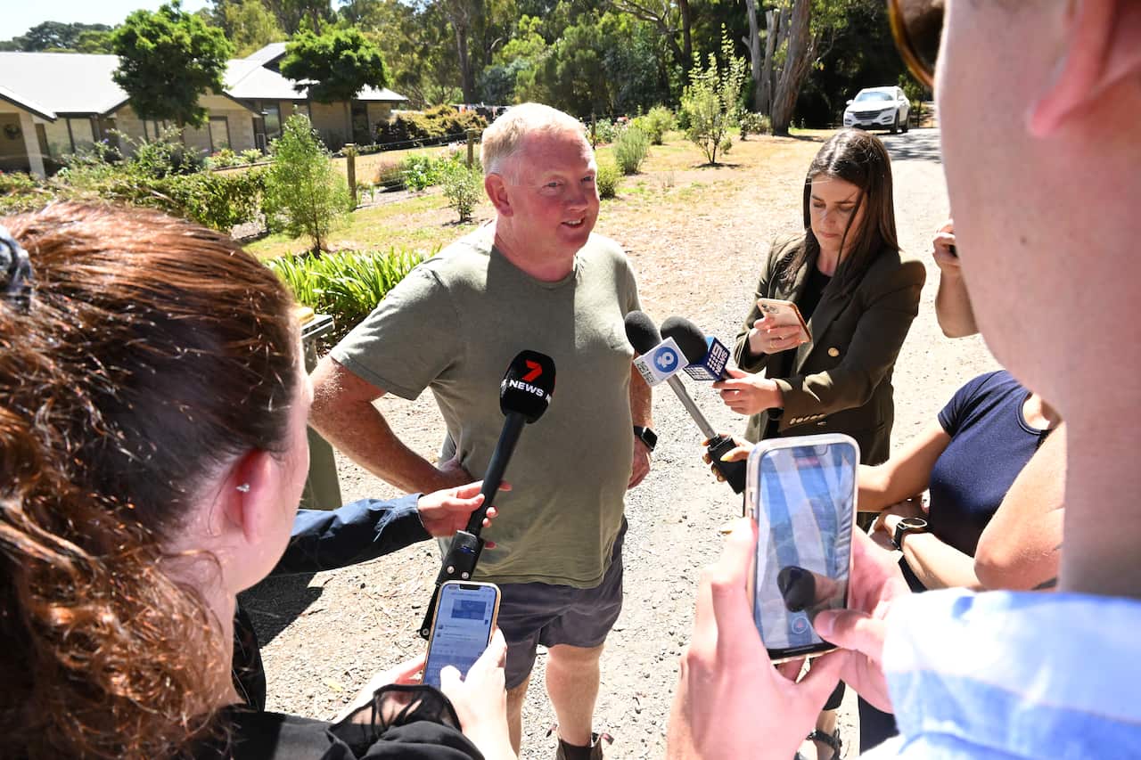 A man standing outside talking to journalists who are holding micophones.
