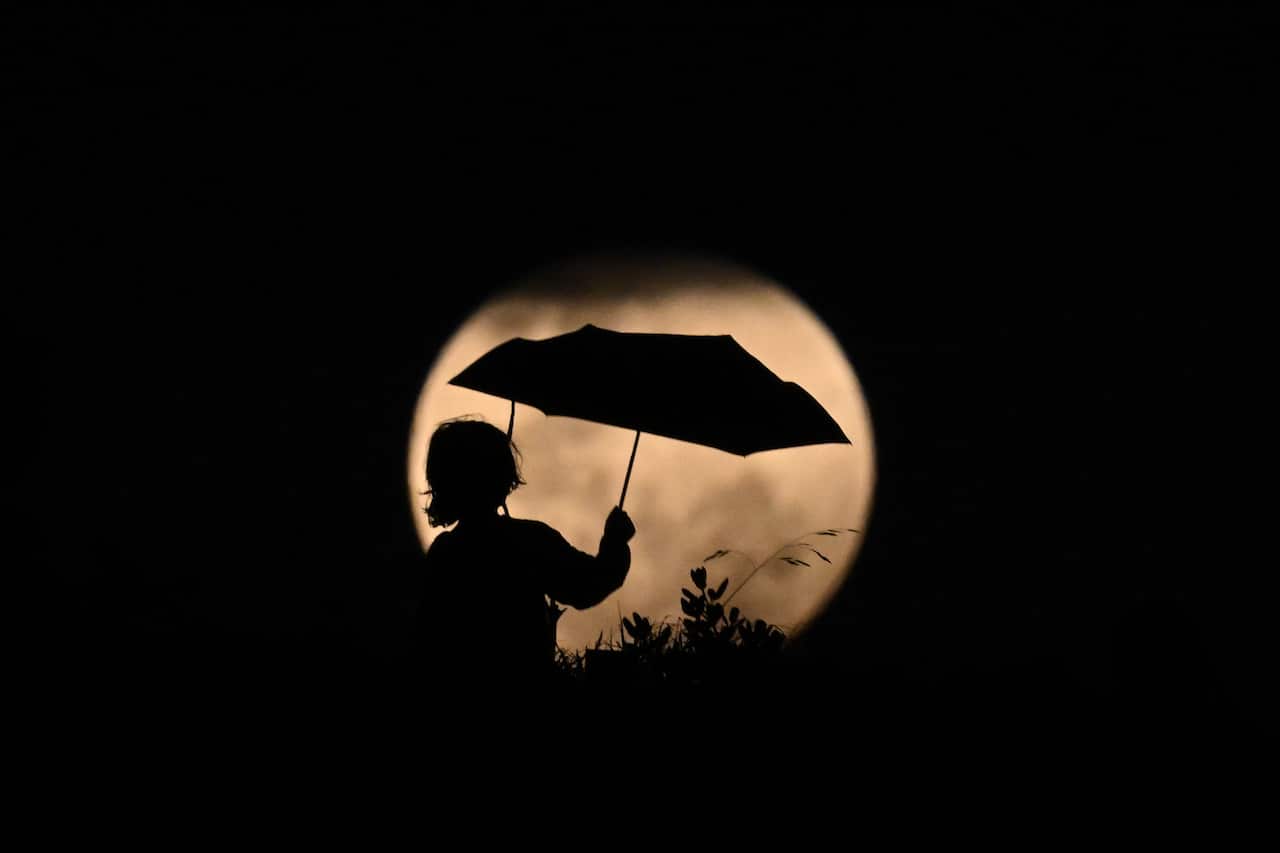 Silhouette of a child holding an umbrella in front of the Moon during an eclipse.