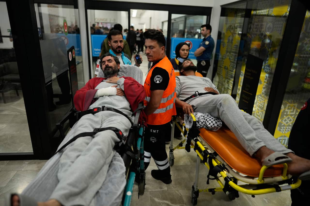 Two patients on stretchers are wheeled through a busy indoor facility by medical personnel and emergency responders.