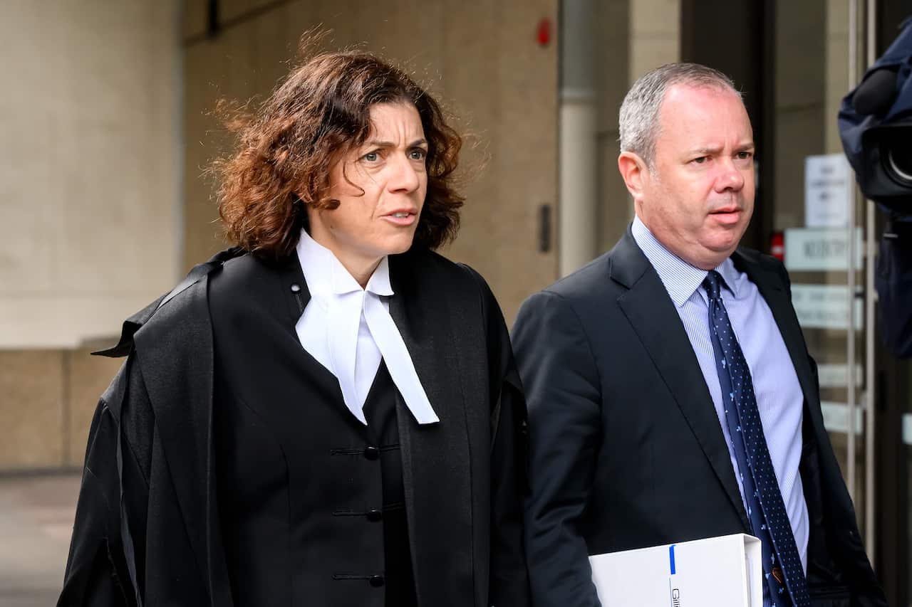 A female lawyer wearing a robe walking next to a man in a suit.