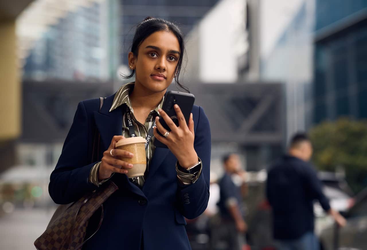 A woman wearing a suit walking in the street and holding a phone.